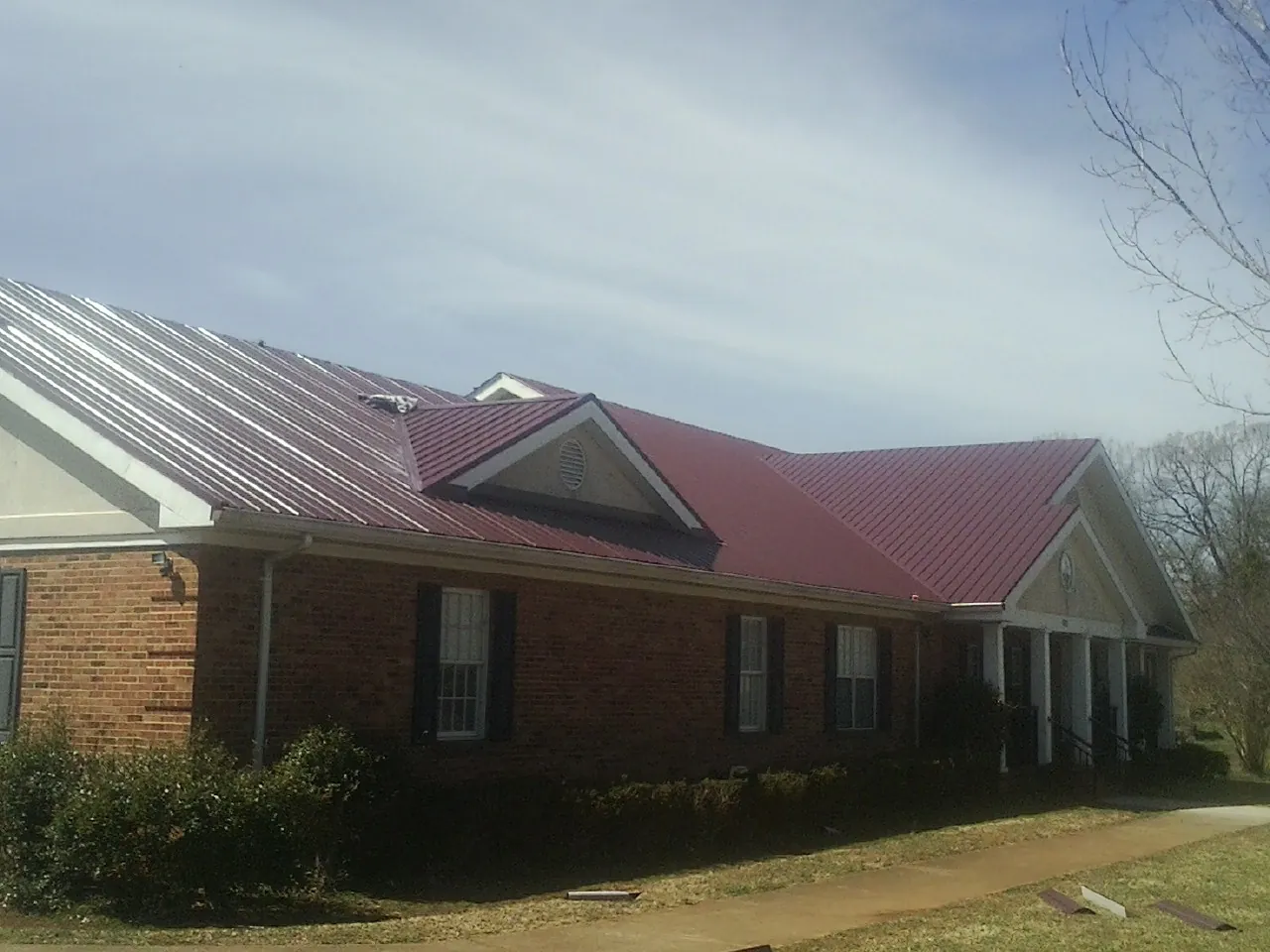 Red metal roof with gabled entries on a long brick building, from a Hail Damage Roof Repair job in Randolph