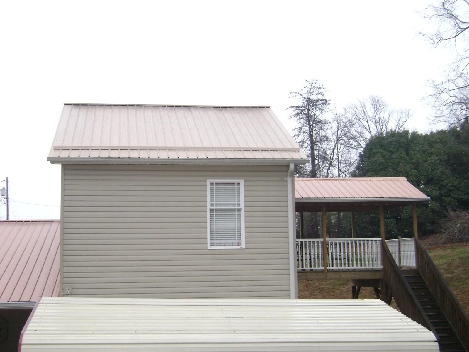 Tan metal roofs on a two story addition and attached porch, from a Roof Replacement job in Randolph